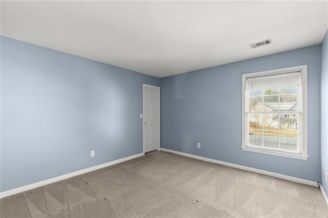 carpeted empty room featuring visible vents, a textured ceiling, and baseboards