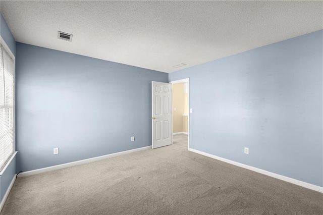 unfurnished room with visible vents, carpet flooring, a textured ceiling, and baseboards