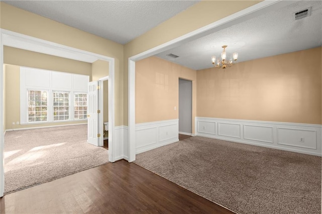 carpeted spare room featuring a notable chandelier, wainscoting, visible vents, and a textured ceiling