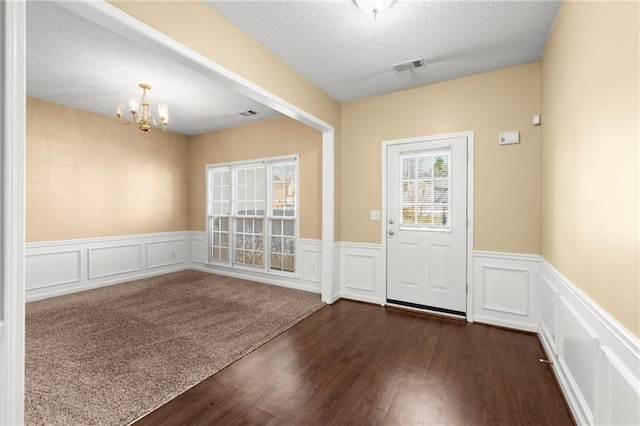 entrance foyer featuring a textured ceiling, dark wood-type flooring, visible vents, and a chandelier