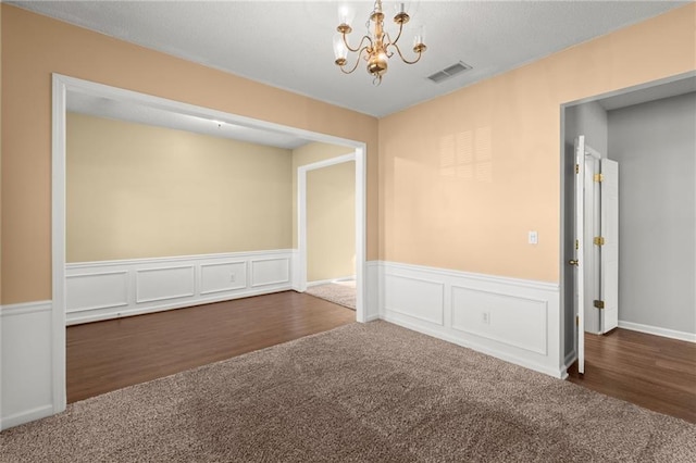 empty room featuring visible vents, a notable chandelier, wainscoting, and dark carpet