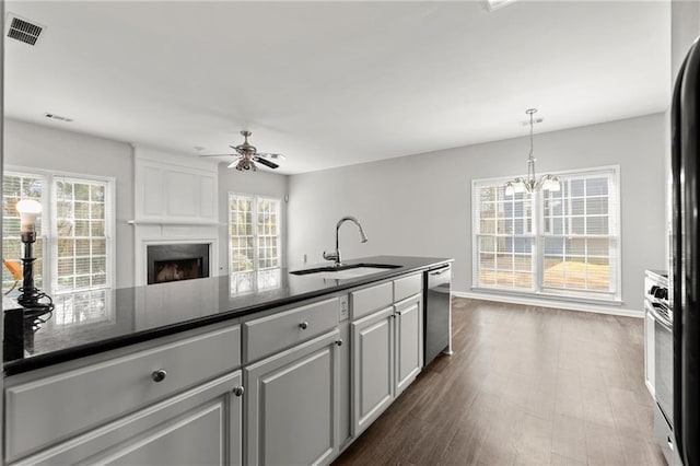 kitchen featuring visible vents, a large fireplace, dishwasher, ceiling fan with notable chandelier, and a sink