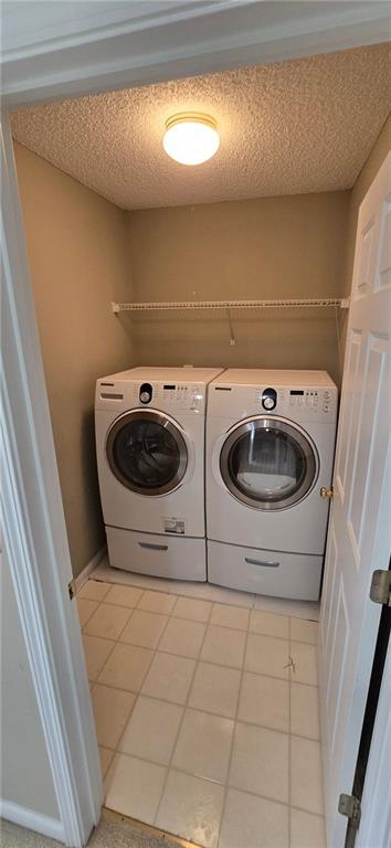 laundry area with a textured ceiling, laundry area, light tile patterned floors, and washer and dryer