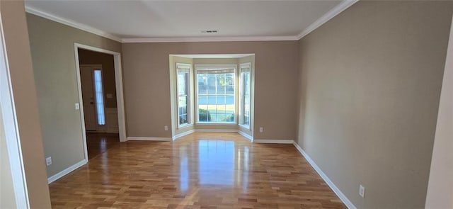 empty room featuring ornamental molding, light wood finished floors, and baseboards