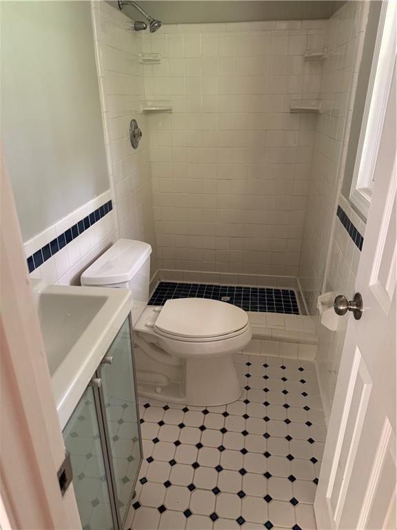 bathroom with tile walls, tile patterned floors, toilet, and tiled shower