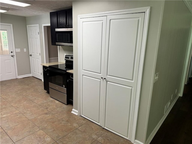 kitchen featuring light tile patterned flooring, a textured ceiling, and appliances with stainless steel finishes