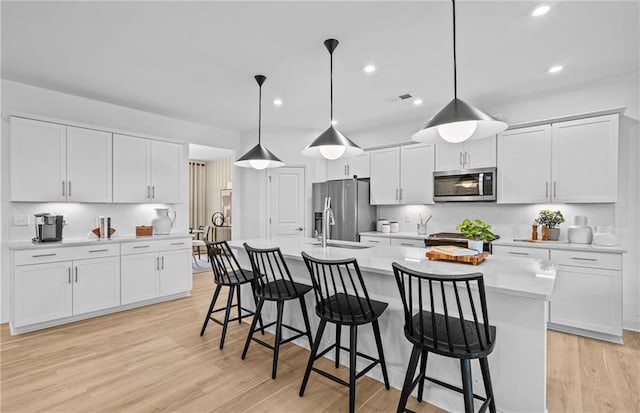 352 Foxglove Way, Mcdonough, GA 30253 - kitchen featuring appliances with stainless steel finishes, white cabinetry, a sink, light wood-style flooring, and a breakfast bar