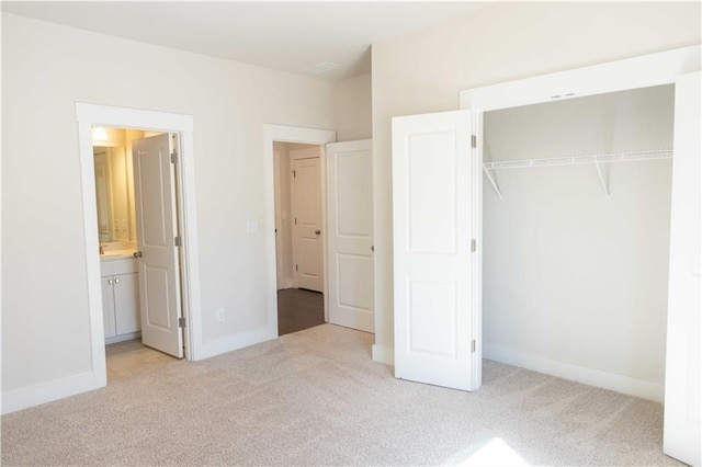 unfurnished bedroom with a closet, light colored carpet, and ensuite bath