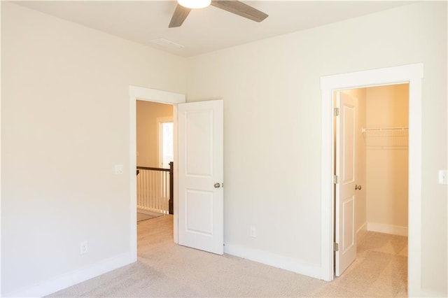 unfurnished bedroom with light carpet, ceiling fan, a closet, and a walk in closet