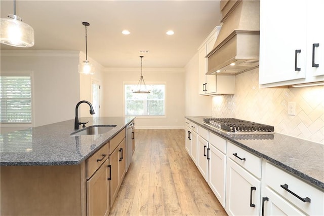 kitchen with crown molding, premium range hood, stainless steel appliances, and a sink