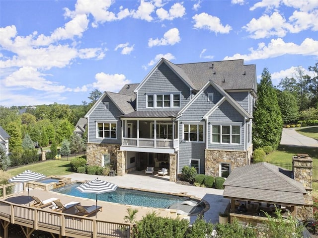 rear view of house with a balcony, a gazebo, a swimming pool with hot tub, and a patio