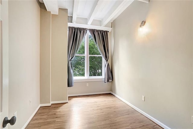 empty room with beamed ceiling and light hardwood / wood-style floors