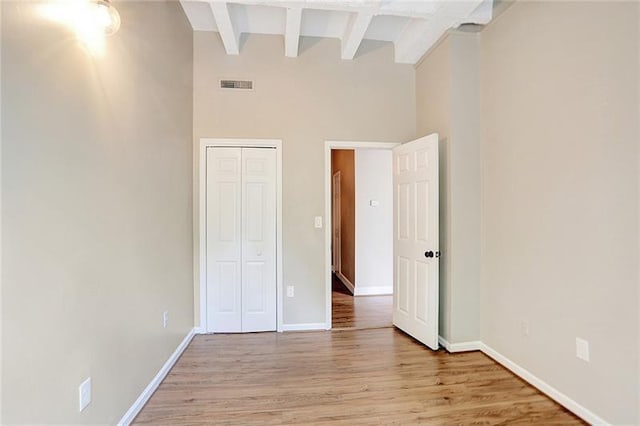 unfurnished bedroom featuring beamed ceiling, a towering ceiling, and light hardwood / wood-style flooring