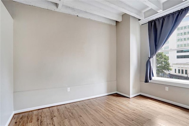 empty room featuring beamed ceiling and light hardwood / wood-style flooring