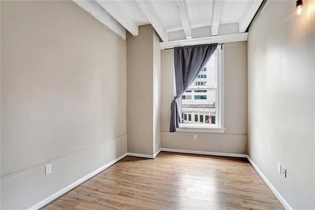 empty room with light hardwood / wood-style flooring and beamed ceiling