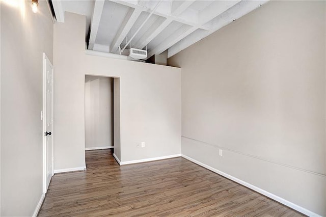 unfurnished room with beamed ceiling, dark hardwood / wood-style floors, and a towering ceiling