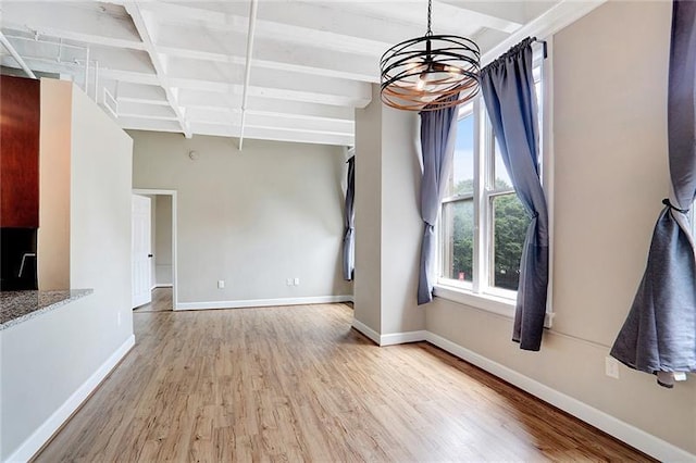 unfurnished dining area featuring light hardwood / wood-style floors, a chandelier, and beamed ceiling