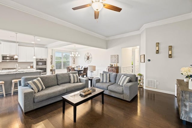 living room featuring visible vents, ornamental molding, baseboards, dark wood finished floors, and ceiling fan with notable chandelier