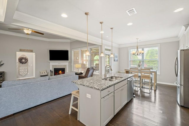 kitchen featuring visible vents, open floor plan, a lit fireplace, a sink, and appliances with stainless steel finishes