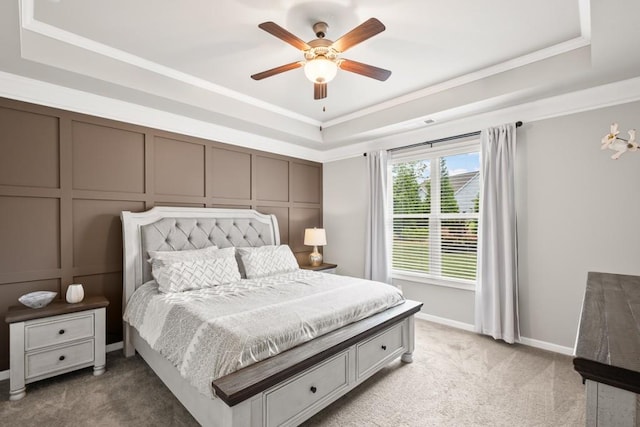 bedroom with a tray ceiling, light carpet, ornamental molding, and a decorative wall