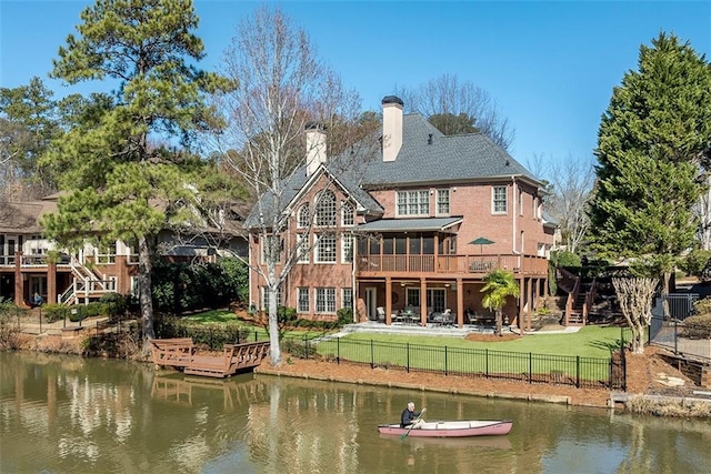 rear view of property featuring a yard, a deck with water view, and a sunroom