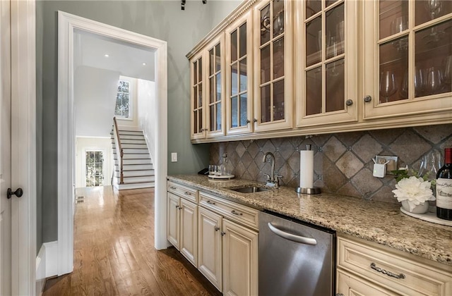 kitchen featuring dark wood-type flooring, stainless steel dishwasher, light stone counters, backsplash, and sink