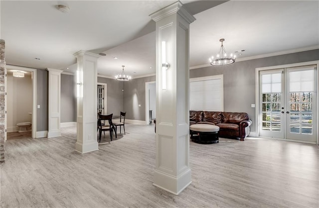 living room with light hardwood / wood-style floors, french doors, ornate columns, ornamental molding, and a chandelier