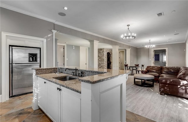 kitchen featuring light stone counters, stainless steel fridge with ice dispenser, a center island with sink, white cabinetry, and ornate columns