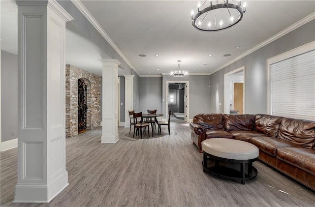 living room featuring ornamental molding, a chandelier, decorative columns, and light hardwood / wood-style flooring