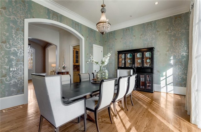 dining space with ornamental molding, light hardwood / wood-style floors, and an inviting chandelier