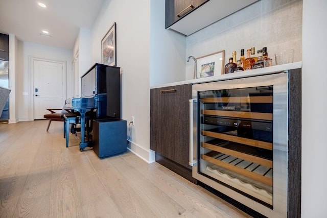 bar with light wood finished floors, baseboards, bar, wine cooler, and recessed lighting