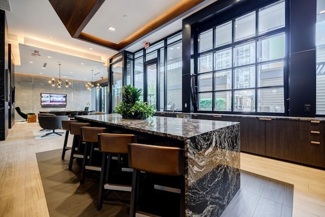 bar featuring light wood-style flooring, a chandelier, pendant lighting, and a tray ceiling