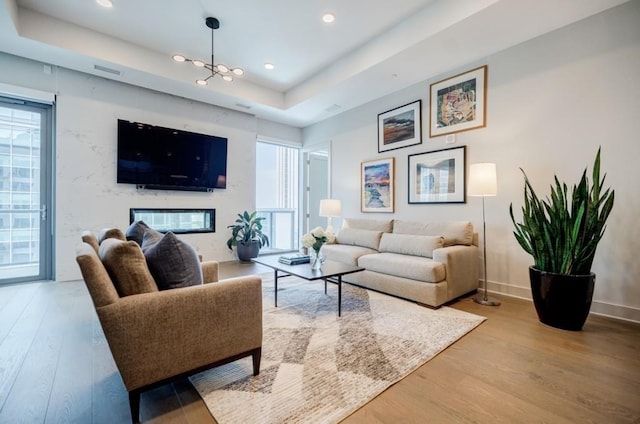 living area with a raised ceiling, visible vents, a high end fireplace, wood finished floors, and baseboards