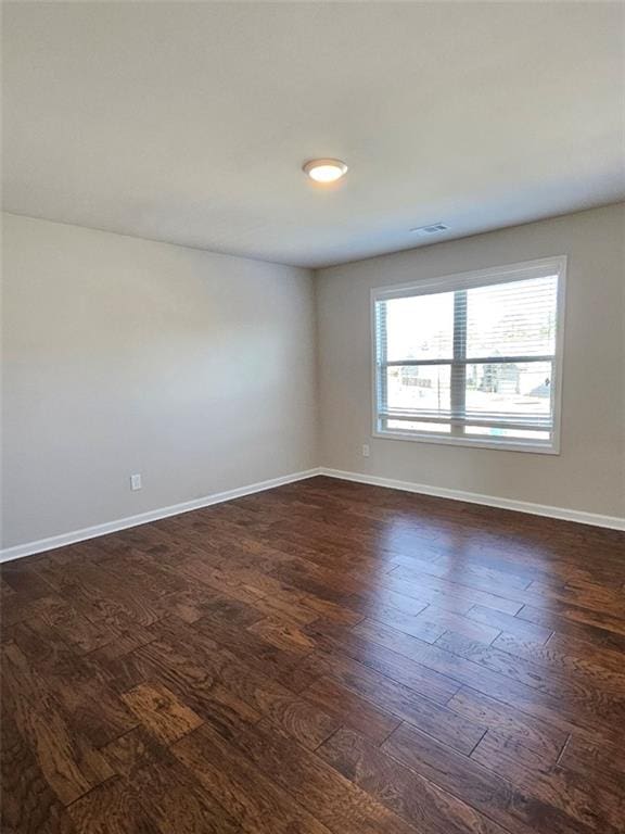 spare room featuring dark wood-style floors, visible vents, and baseboards