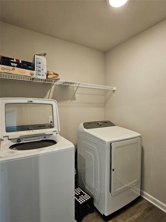 clothes washing area featuring dark wood finished floors, laundry area, baseboards, and separate washer and dryer