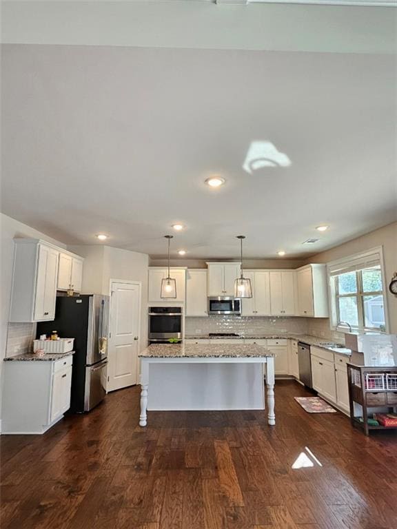 kitchen featuring dark wood-type flooring, a kitchen island, white cabinetry, appliances with stainless steel finishes, and a breakfast bar area