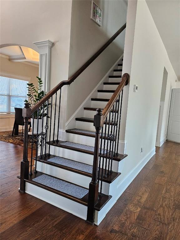 stairway featuring decorative columns, wood finished floors, baseboards, and arched walkways