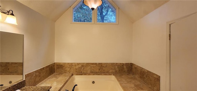 bathroom with vanity, a relaxing tiled tub, and vaulted ceiling