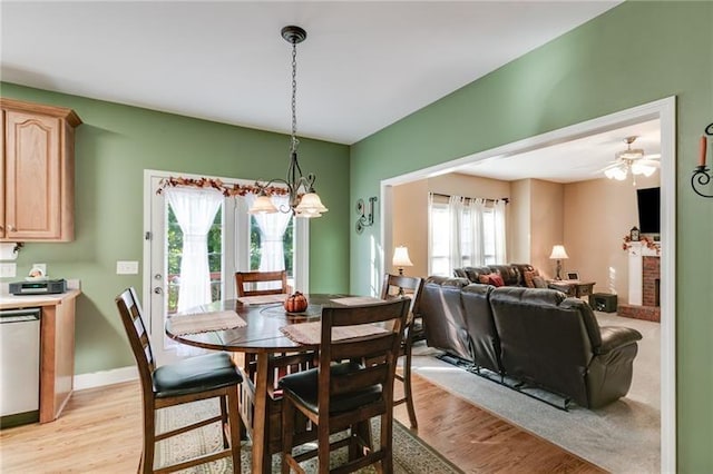 dining area with ceiling fan with notable chandelier, light wood finished floors, a brick fireplace, and baseboards