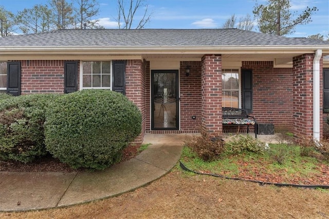 property entrance with a shingled roof and brick siding