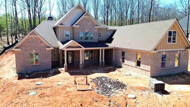 view of front of house with brick siding, board and batten siding, a shingled roof, and covered porch