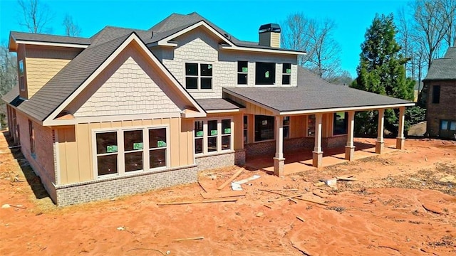 rear view of property with board and batten siding, a shingled roof, a chimney, and brick siding