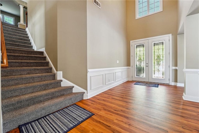 foyer featuring wood finished floors, visible vents, french doors, wainscoting, and stairs