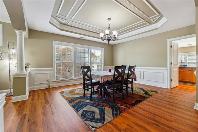 dining area featuring light wood finished floors, ornate columns, a decorative wall, wainscoting, and a notable chandelier