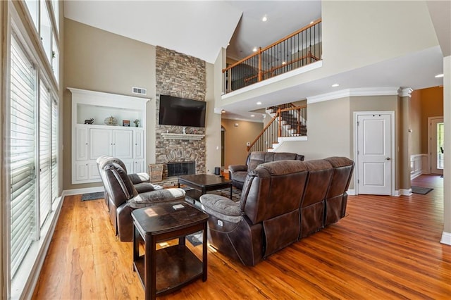 living room with a stone fireplace, wood finished floors, baseboards, a high ceiling, and visible vents