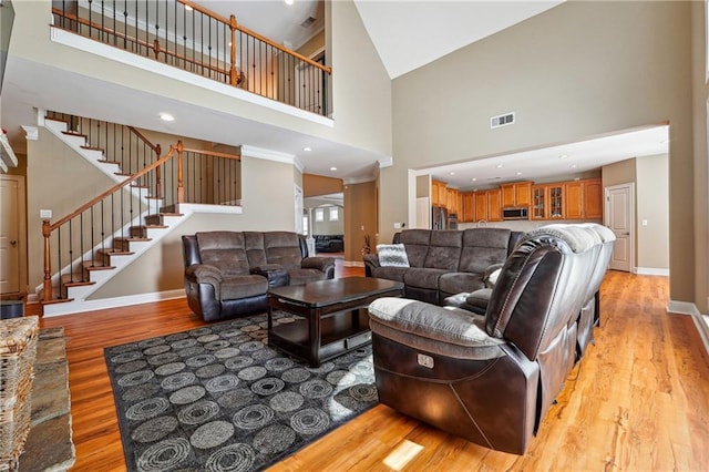 living area featuring light wood-type flooring, baseboards, visible vents, a high ceiling, and stairs