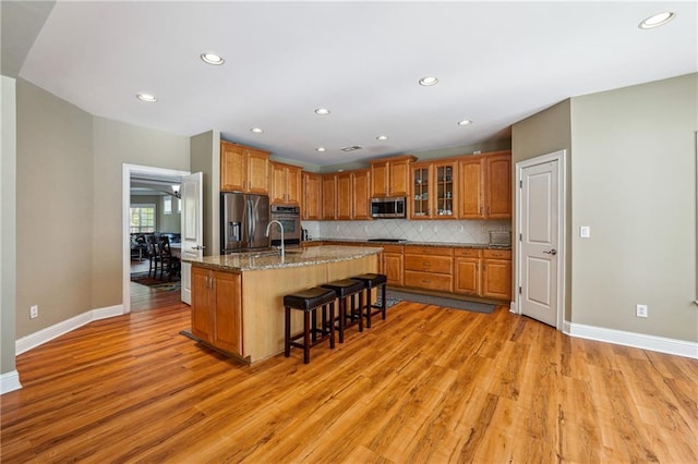 kitchen featuring light wood-type flooring, brown cabinetry, a breakfast bar area, and appliances with stainless steel finishes