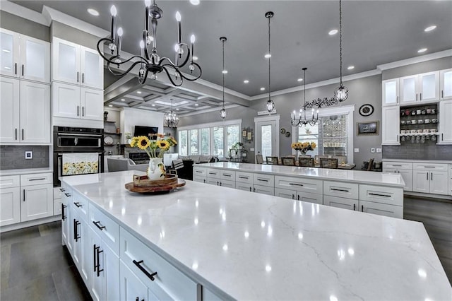 kitchen featuring dark wood-type flooring, double oven, light stone counters, decorative light fixtures, and backsplash