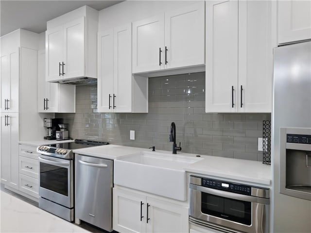 kitchen featuring stainless steel appliances, tasteful backsplash, light stone countertops, white cabinets, and sink