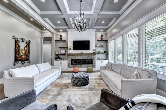 living room featuring crown molding, built in features, a premium fireplace, a chandelier, and coffered ceiling